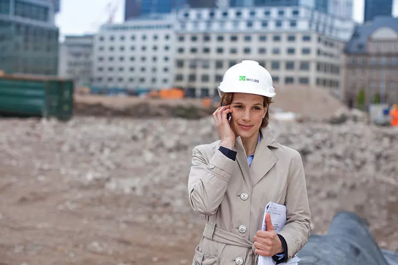 WISAG Mitarbeiterin telefoniert vor Baustelle