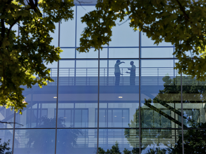 Zwei Personen unterhalten sich im Gebäude hinter einer Glasfassade