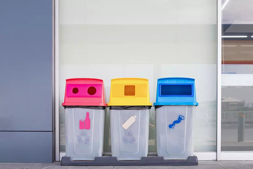 Drei verschiedenfarbige Abfalltonnen vor einer Wand