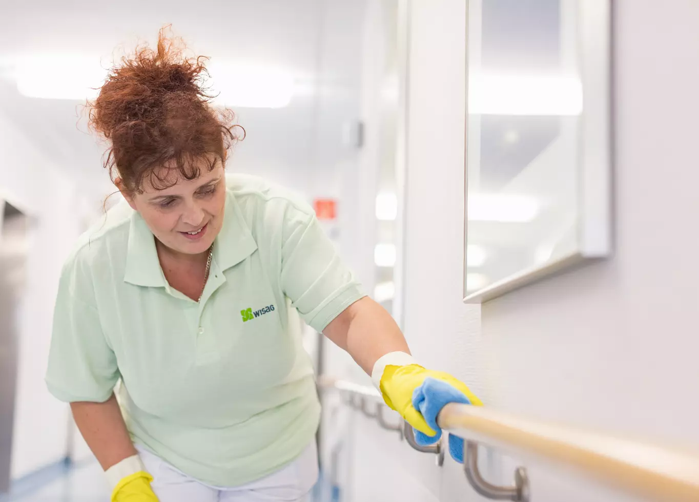 WISAG Mitarbeiterin beim Reinigen des Geländers in einem Krankenhausflur