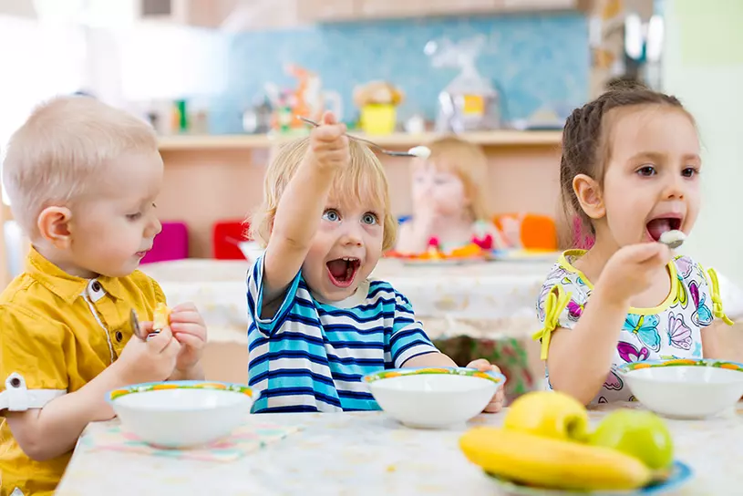 Drei Kinder sitzen am Tisch und essen mit Freude