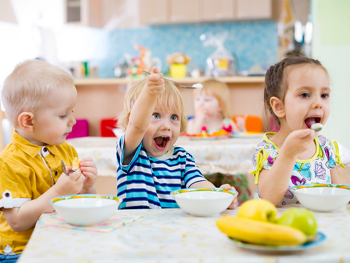 Drei Kinder sitzen am Tisch und essen mit Freude