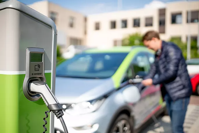 Elektroladesäule im Vordergrund und Auto mit Fahrer im Hintergrund