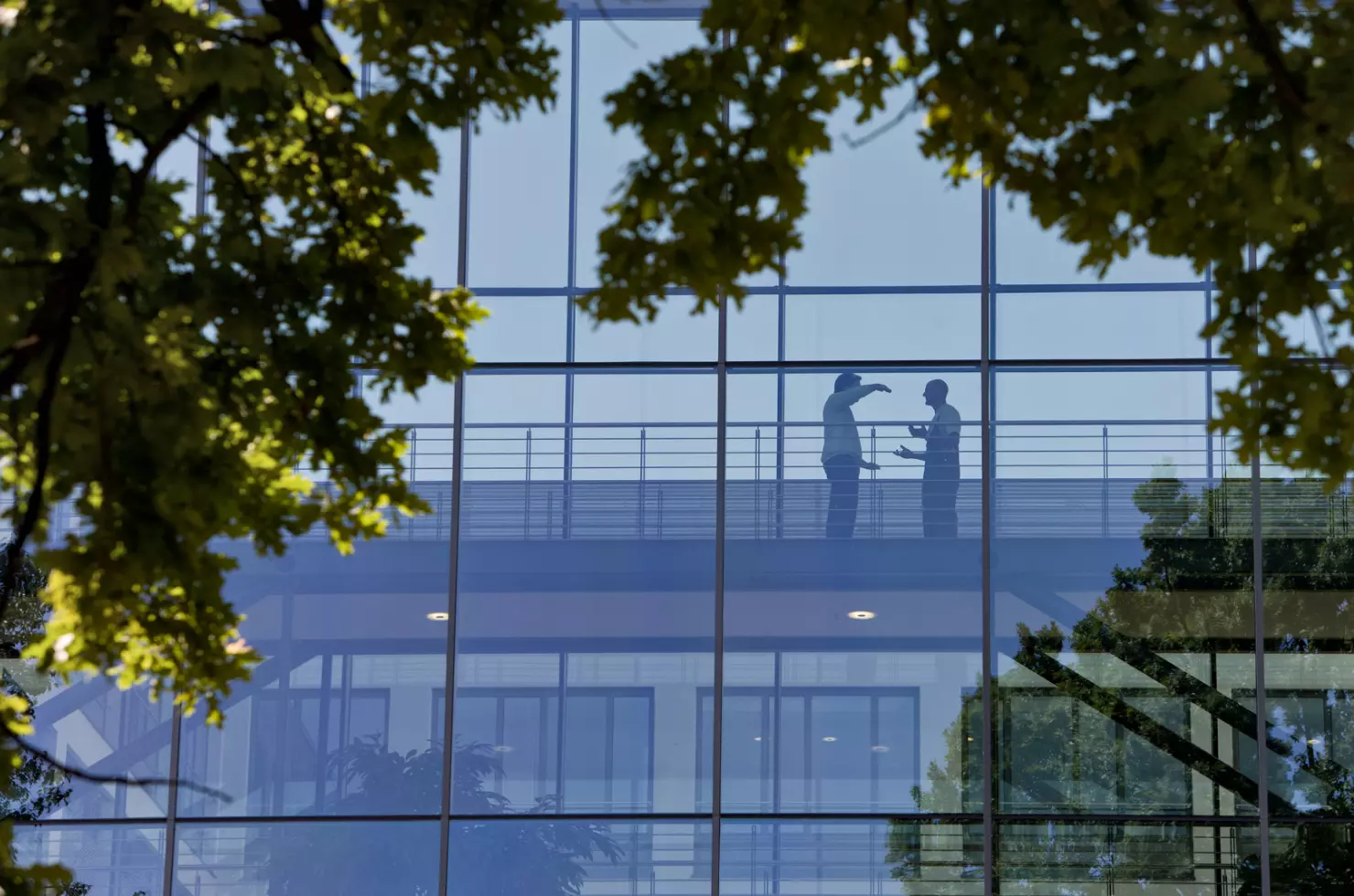 Zwei Personen unterhalten sich im Gebäude hinter einer Glasfassade